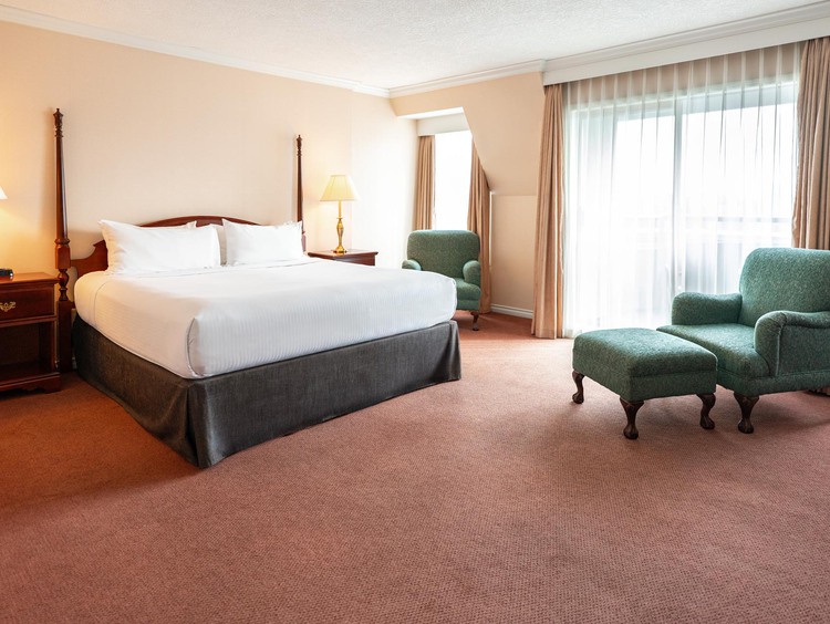 A guest room with a king bed and green armchairs