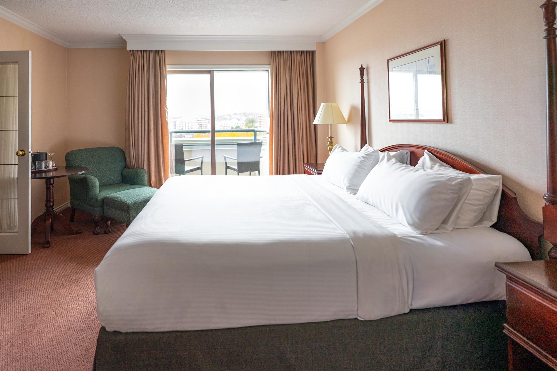 A king bed beside a large window and a green armchair