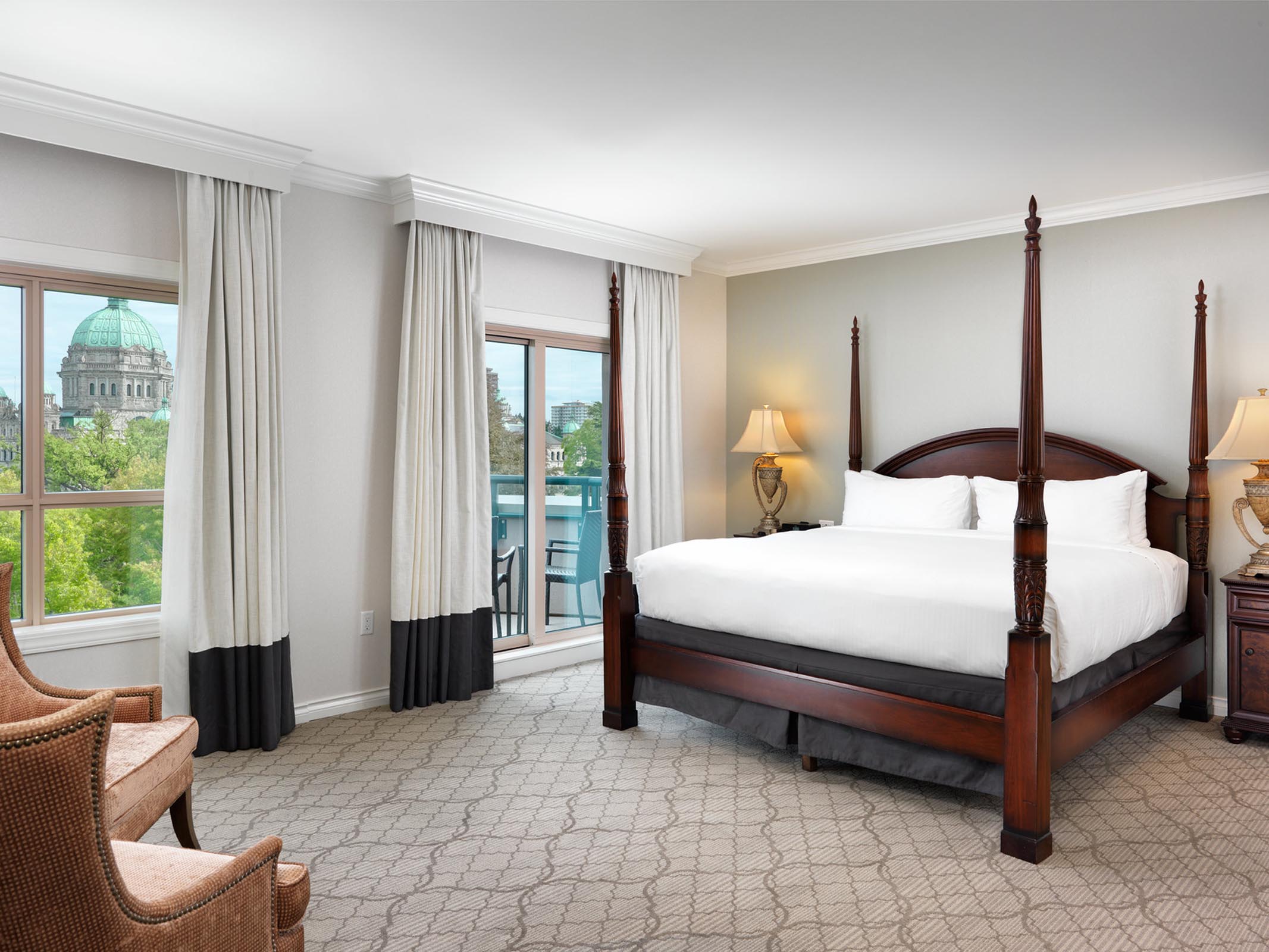 King bed with brown pillars, chair, and sliding doors to balcony